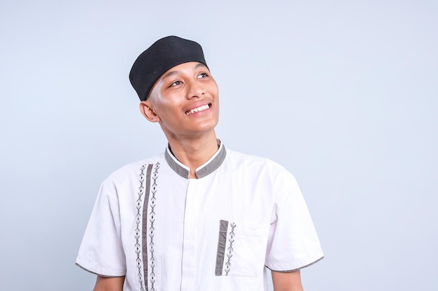 Portret van een vrolijke jonge Aziatische moslimman die een pet draagt en naar boven kijkt met een gelukkige uitdrukking