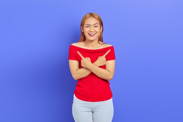 Portret van een vrolijke jonge Aziatische vrouw die staat en wijst om de ruimte te kopiëren met een vinger geïsoleerd op een paarse achtergrond