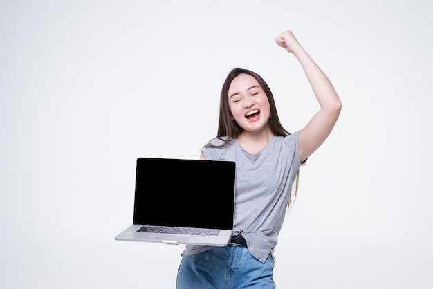 Portret van een vrolijke jonge Aziatische vrouw wijzende vinger op lege scherm laptop geïsoleerd over witte muur