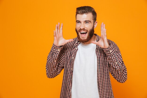 Portret van een vrolijke jonge mens die vrijetijdskleding draagt die zich geïsoleerd over gele muur bevindt, schreeuwt