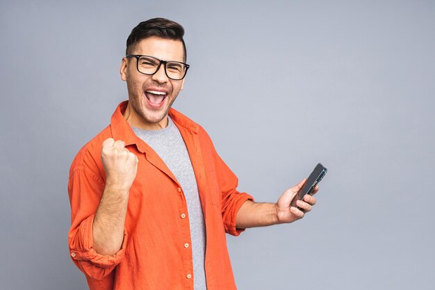 Portret van een vrolijke jonge Oekraïense man met een mobiele telefoon geïsoleerd op een grijze witte achtergrond die de overwinning viert Gelukkige winnaar