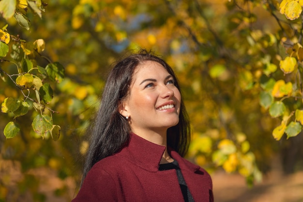 Portret van een vrolijke jonge vrouw die geniet in het herfstpark. Mooie brunette meisje in herfst rode jas en zwarte trui. Ontspan in de natuur. Hoge kwaliteit foto