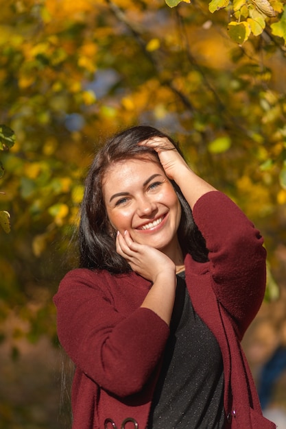 Portret van een vrolijke jonge vrouw die geniet in het herfstpark. Mooie brunette meisje in herfst rode jas en zwarte trui. Ontspan in de natuur. Hoge kwaliteit foto