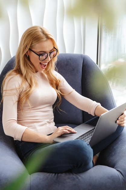 Portret van een vrolijke jonge vrouw die laptop met behulp van