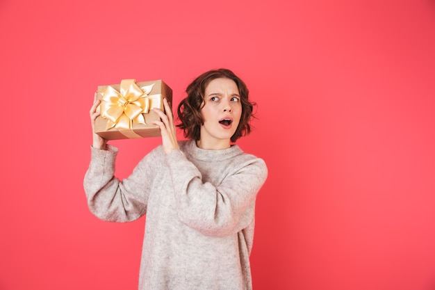 Portret van een vrolijke jonge vrouw die zich geïsoleerd over roze bevindt, die huidige doos houdt