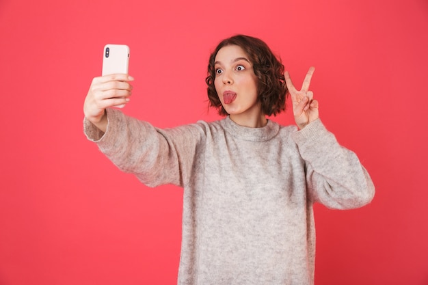 Portret van een vrolijke jonge vrouw die zich geïsoleerd over roze bevindt, een selfie neemt