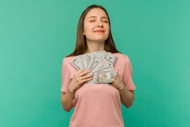 Portret van een vrolijke jonge vrouw met geld bankbiljetten en vieren geïsoleerd op blauwe achtergrond