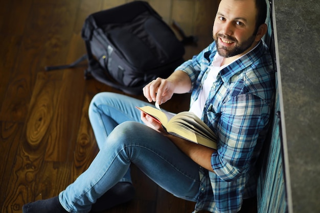 Foto portret van een vrolijke jongeman die een boek leest in zijn woonkamer student die een boek vasthoudt en leest