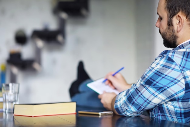 Portret van een vrolijke jongeman die een boek leest terwijl hij op de vloer in zijn woonkamer zit. student houdt en leest boek.