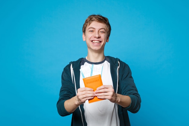 Portret van een vrolijke jongeman in casual kleding houdt paspoort, instapkaart ticket geïsoleerd op blauwe muur muur. mensen oprechte emoties, lifestyle concept.