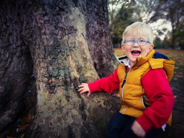 Foto portret van een vrolijke jongen die op zijn knieën ligt bij een boomstam in het park