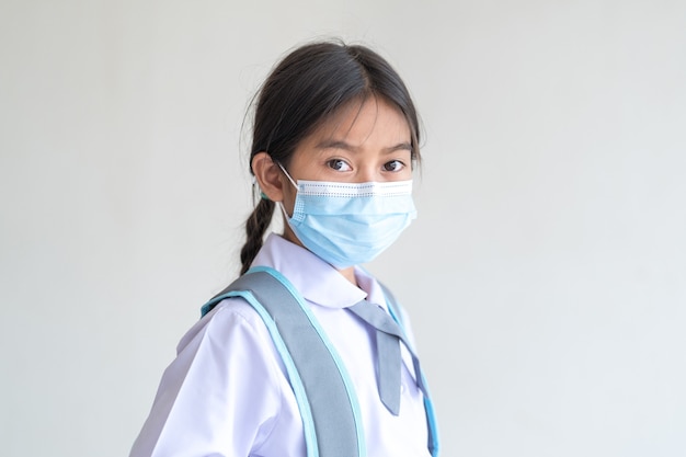 Portret van een vrolijke kind student draagt een gezichtsmasker geïsoleerd op een witte achtergrond glimlacht en kijkt naar de camera. Terug naar school concept Stock Photo