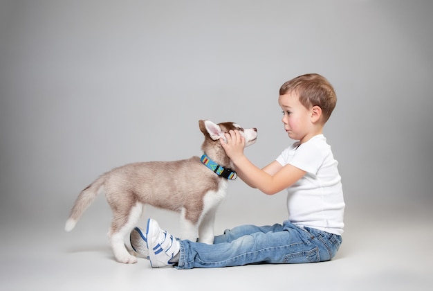 Portret van een vrolijke kleine jongen die plezier heeft met siberische husky puppy op de vloer in de studio