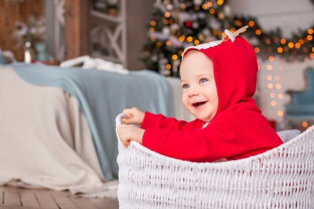 Portret van een vrolijke kleine kinderen in een rood rendierkostuum van de kerstman die in de mand zit tegen de achtergrond van de kerstboom