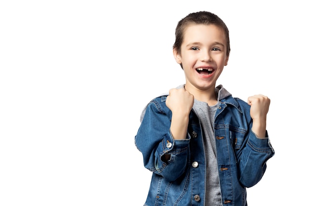 Portret van een vrolijke lachende jongen in denim jasje met vuisten en vreugde over zijn prestaties en overwinning op witte geïsoleerde achtergrond