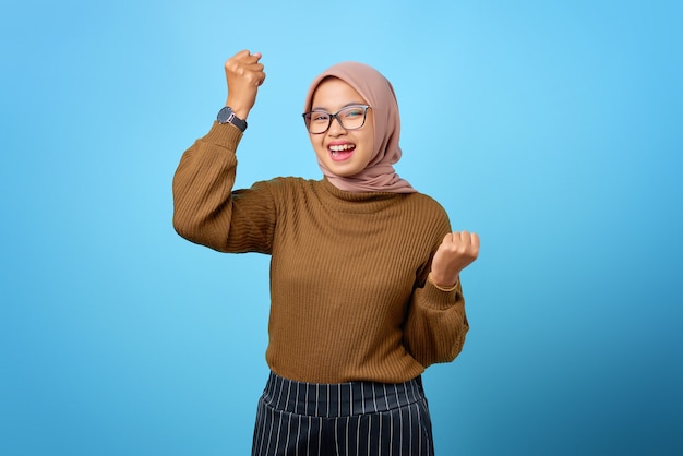 Portret van een vrolijke mooie Aziatische vrouw die zich verheugt over het vieren van geluk op een blauwe achtergrond