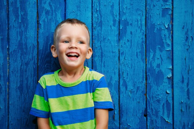 Portret van een vrolijke, mooie kleine jongen tegen de oude getextureerde blauwe muur blue