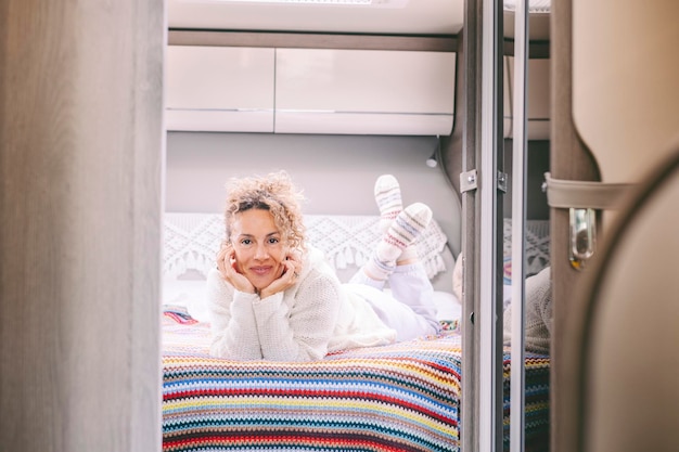Portret van een vrolijke, mooie volwassen vrouw die in haar camper in de slaapkamer ligt en glimlacht Concept van reizen en leven van mensen op het rooster