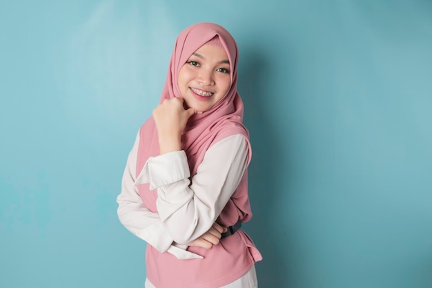 Portret van een vrolijke moslim Aziatische vrouw die staat en lacht naar de camera geïsoleerd op een blauwe achtergrond