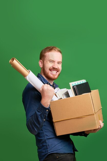 Portret van een vrolijke opgewonden jonge blanke man die een spullendoos vasthoudt en een ja-gebaar maakt terwijl hij van baan verandert