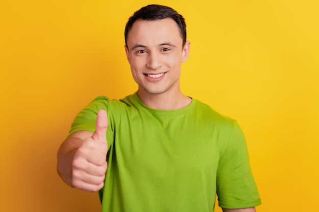 Portret van een vrolijke positieve kerel die een glimlach uitstraalt, duim omhoog op gele achtergrond