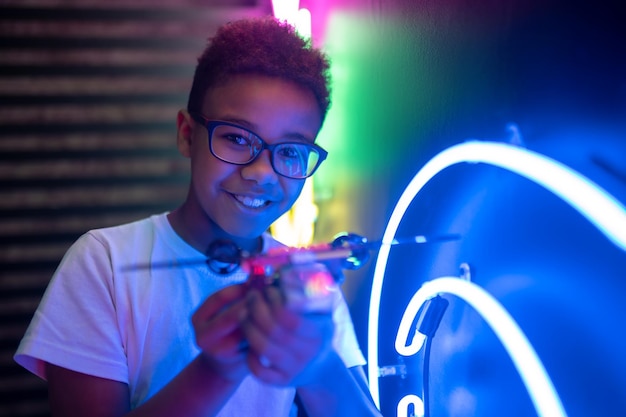 Foto portret van een vrolijke schattige tiener met een bril die een speelgoedhelikopter in zijn handen houdt en vooruitkijkt