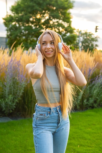 Portret van een vrolijke stijlvolle jonge vrouw die naar de muziek luistert met koptelefoon in het park