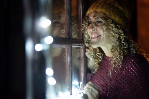 Portret van een vrolijke vrouw die thuis in de winter naar buiten kijkt