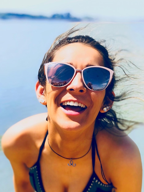 Portret van een vrolijke vrouw met een zonnebril op het strand op een zonnige dag