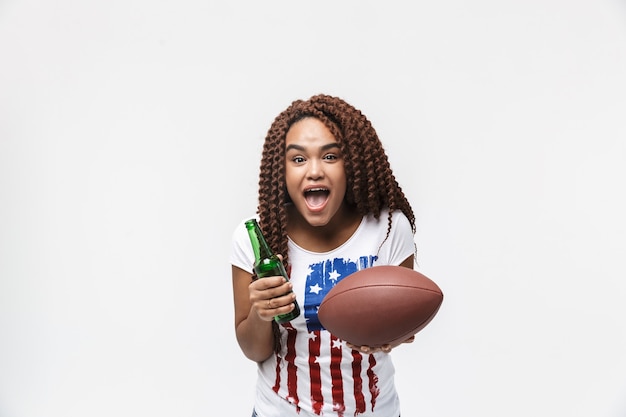 Portret van een vrolijke vrouw met rugbybal en bierflesje tijdens het spel geïsoleerd tegen een witte muur