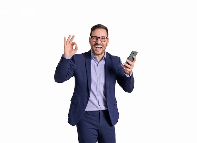 Portret van een vrolijke zakenman met een mobiele telefoon die schreeuwt en een OK-bord op een witte achtergrond toont