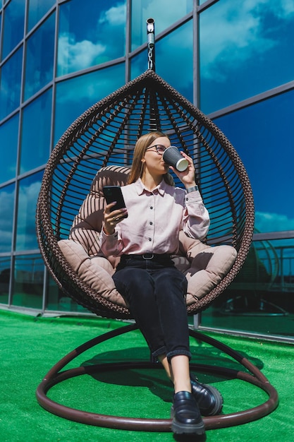 Portret van een vrolijke zakenvrouw in glazen die op een zonnige dag buiten een koffiepauze geniet van een succesvolle vrouwelijke manager die aan de telefoon praat terwijl hij tegen de achtergrond van het kantoor zit