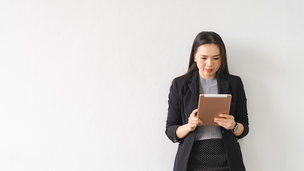 Portret van een vrolijke zelfverzekerde Aziatische zakenvrouw in een pak dat staat met een digitale tablet in het bedrijfsgebouw. Zakelijke stockfoto