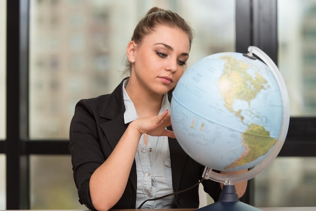 Portret van een vrouw die bij haar bureau zit en een wereldbolmodel vasthoudt