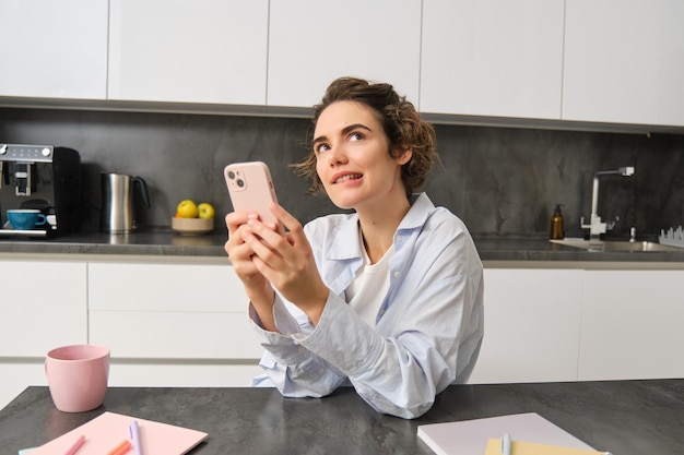 Portret van een vrouw die denkt terwijl ze een smartphone vasthoudt en besluit wat ze moet bestellen via de mobiele-telefoonapp