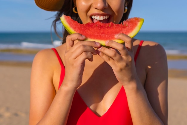 Portret van een vrouw die een watermeloen eet aan het strand Knipsel van lachende mond met rode bikini