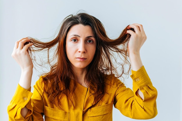 Foto portret van een vrouw die handen lang haar vasthoudt en er ongelukkig uitziet, rommelig haar brunette vrouw met messed