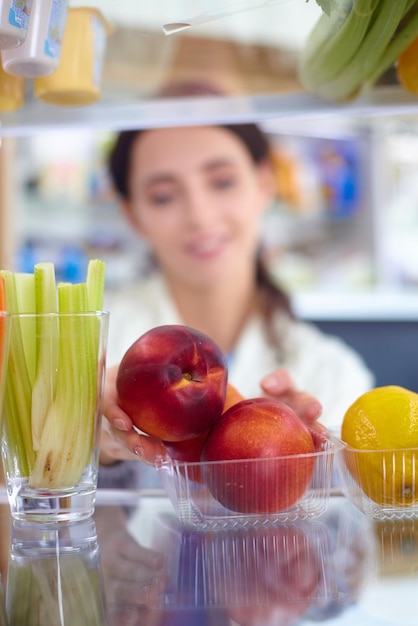 Portret van een vrouw die in de buurt van een open koelkast staat vol gezonde groenten en fruit