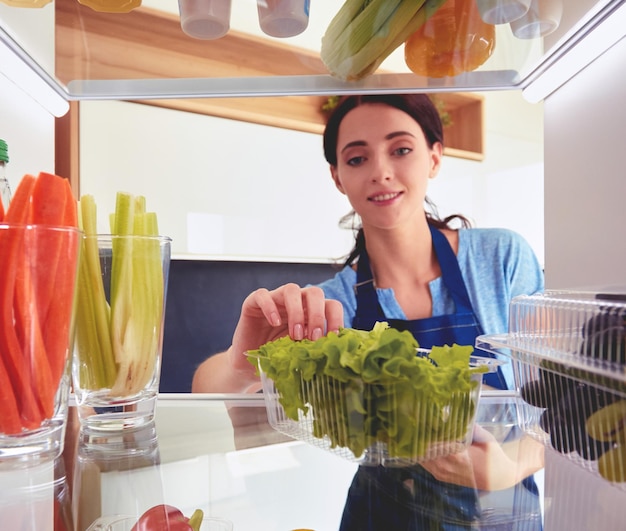 Portret van een vrouw die in de buurt van een open koelkast staat vol gezonde groenten en fruit