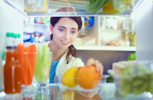 Portret van een vrouw die in de buurt van een open koelkast staat vol gezonde voeding, groenten en fruit. Portret van een vrouw.