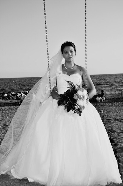 Foto portret van een vrouw die in een schommel op het strand tegen de lucht zit