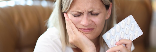 Portret van een vrouw die lijdt aan kiespijn en pijnstillers in de hand houdt. Kiespijn tandheelkundige gezondheid