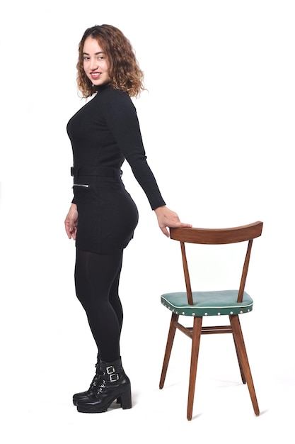 Portret van een vrouw die met een stoel op een witte achtergrond staat en naar de camera kijkt