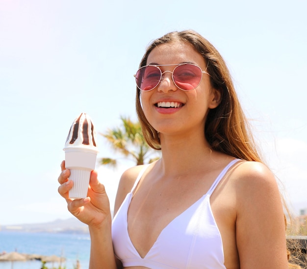 Portret van een vrouw die met zonnebril van ijs op het strand eet