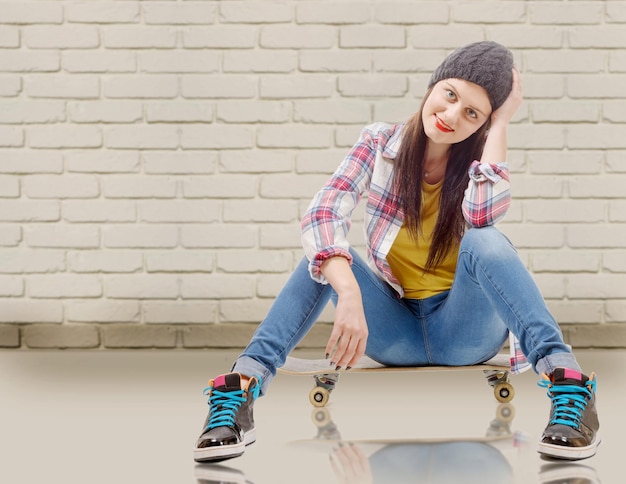 Foto portret van een vrouw die op een skateboard tegen een bakstenen muur zit
