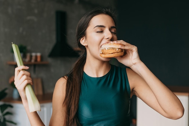 Portret van een vrouw die thuis een hamburger bijt en een sportkleding draagt, een gezond levensstijlconcept, gezond voedsel