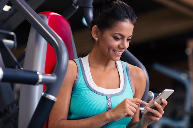 Portret van een vrouw gelukkig fitness met behulp van smartphone in de sportschool