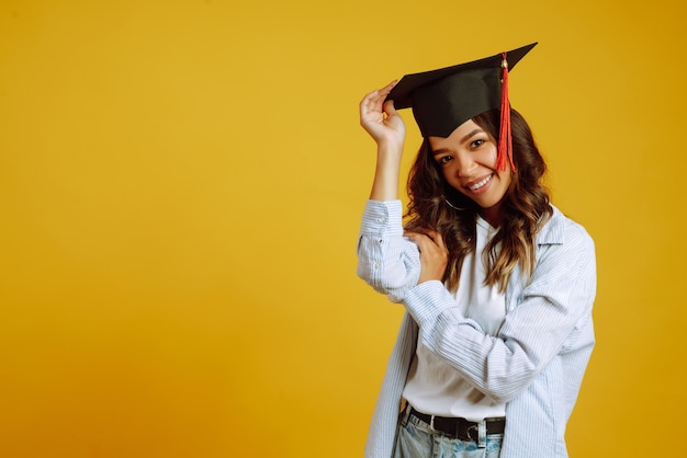 Portret van een vrouw in een afstuderen hoed op haar hoofd poseren op geel.