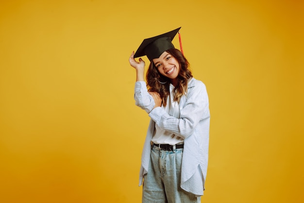 Portret van een vrouw in een afstuderen hoed op haar hoofd poseren op geel.