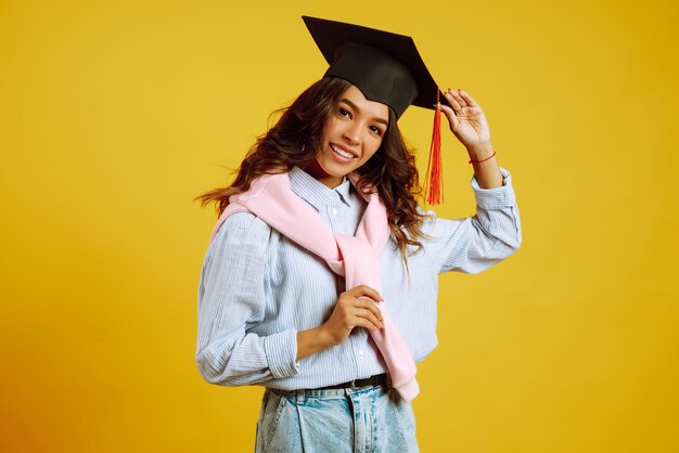 Portret van een vrouw in een afstuderen hoed op haar hoofd poseren op geel.